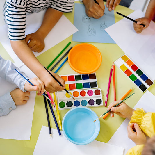 Crianças ao redor de uma mesa, pintando e desenhando com tintas coloridas.