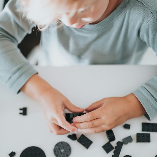 Menino montando lego em uma mesa branca.